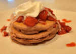 stack of pancakes with strawberry banana sauce and topped with melting whipped cream.