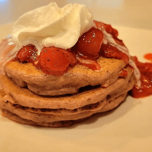 stack of pancakes with strawberry banana sauce and topped with melting whipped cream.