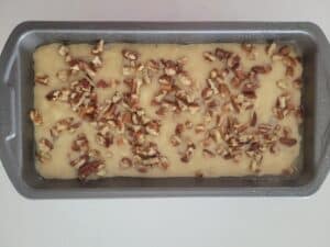 banana bread batter in a loaf pan with chopped pecans sprinkled on top