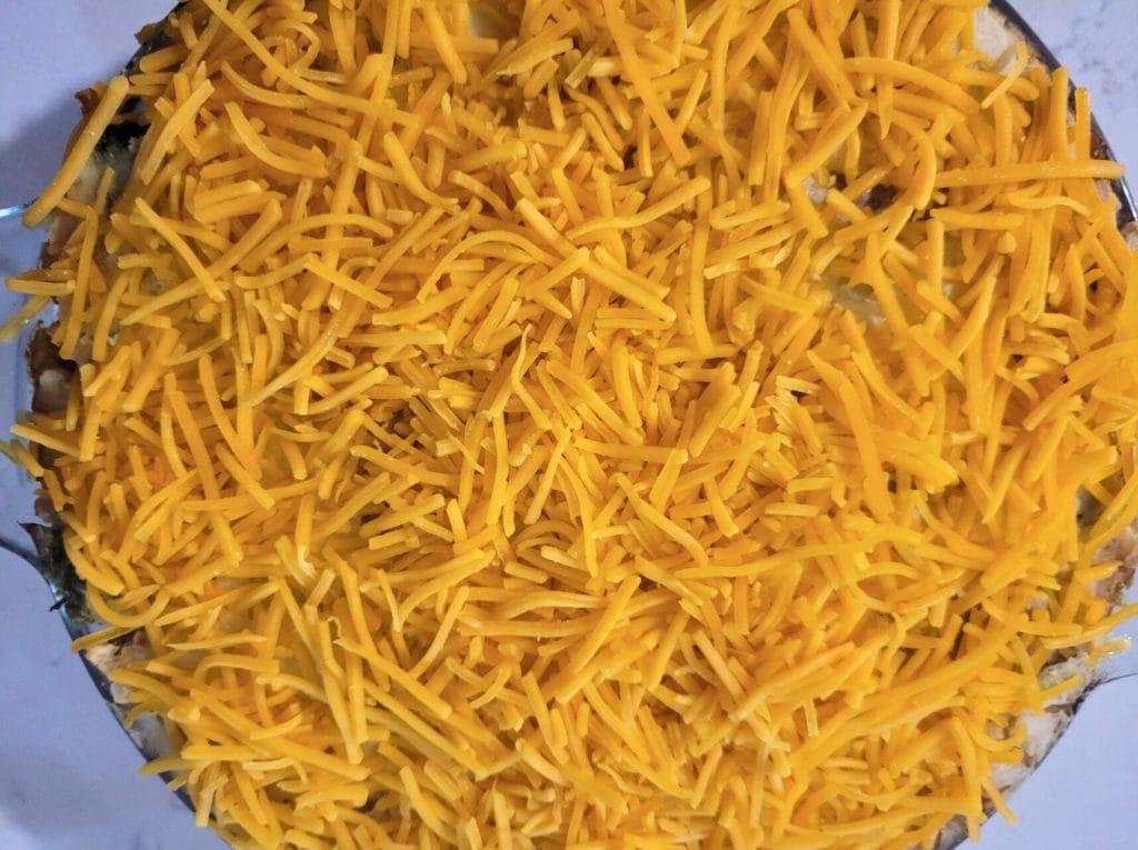 shredded cheddar cheese on top of a guinness shepherd's pie in a glass pie dish