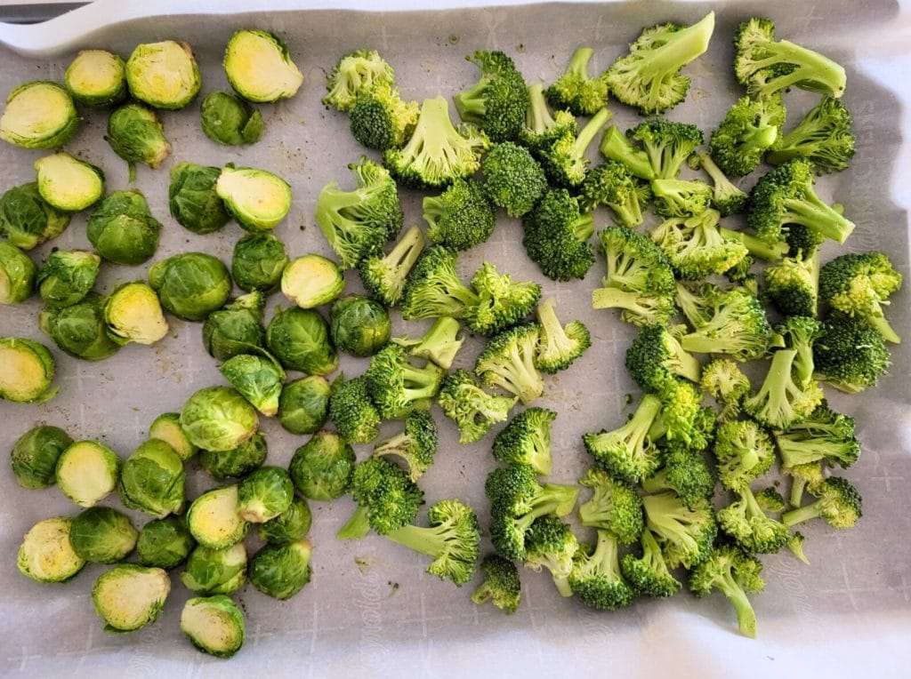 Chopped broccoli and Brussels sprouts on a parchment paper lined baking sheet