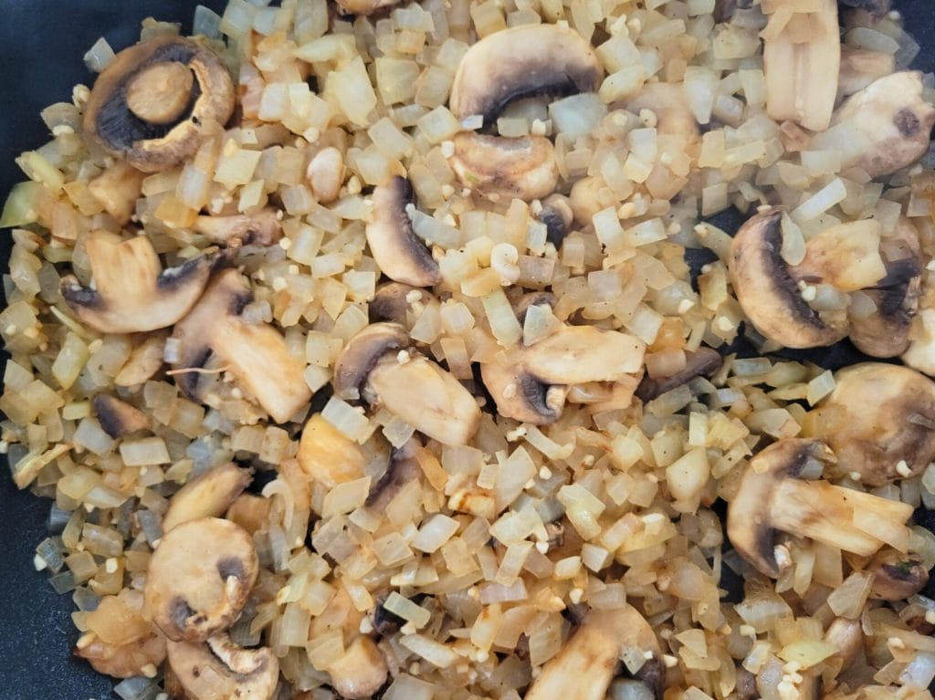 sauteed diced onions, minced garlic, and sliced mushrooms in a black skillet