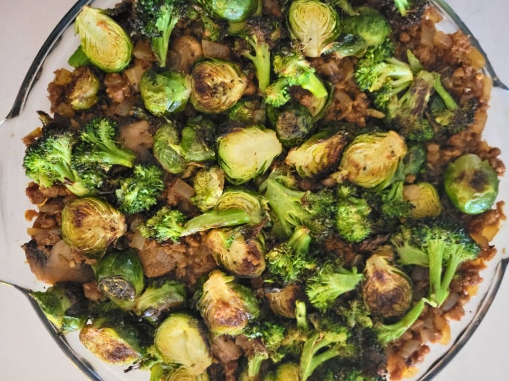 Guinness Shepherd's Pie gravy filling topped with roasted broccoli and Brussels sprouts in a glass pie dish 