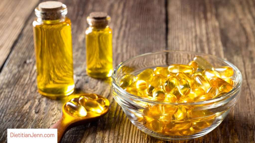 amber oil in 2 vials and as capsules in a clear glass bowl on a wooden surface
