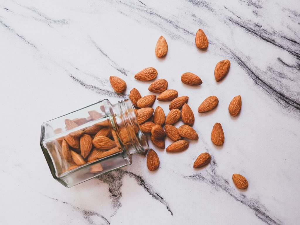 almonds spilling out of a glass jar onto a white marbled surface