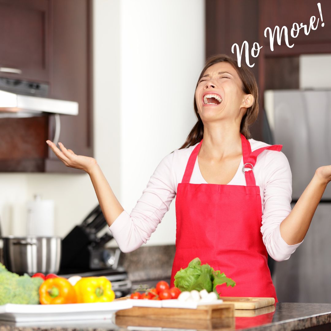 A person in an apron standing in the kitchen with a frustrated face and her hands and face raised