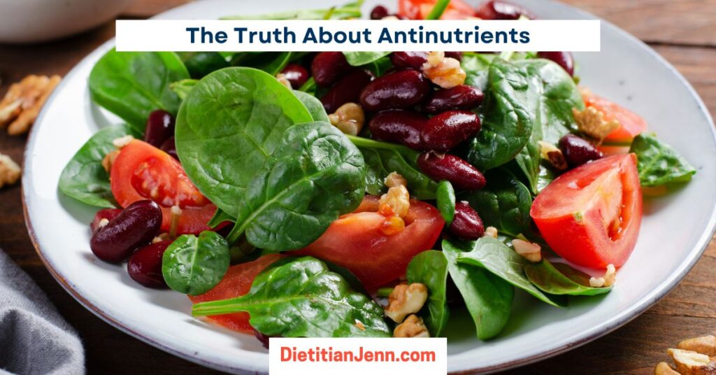 a spinach salad with kidney beans, walnuts, and tomato slices on a white plate. Text above reads, "The Truth About Antinutrients"