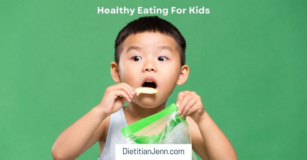 a young boy eating a cracker out of a clear plastic bag with a worried look on his face, against a plain green background. Text above reads, "Healthy Eating For Kids"