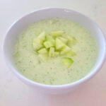 cucumber mint gazpacho in a white bowl, garnished with diced cucumbers, on a white marbled surface.