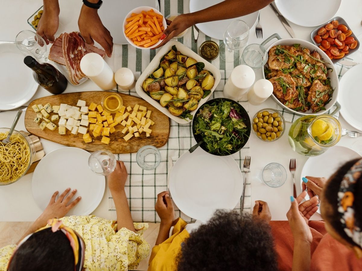 a spread of food served family style including meat and vegetarian options. a family is sitting around the table, with empty plates.
