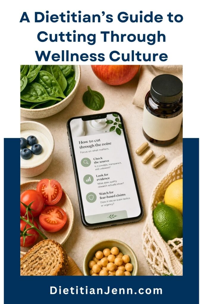 A smartphone displays a guide on how to cut through noise, surrounded by healthy foods like spinach, blueberries, tomatoes, bread, chickpeas, and citrus fruits, along with a bottle of supplements. text above reads, "A Dietitian's Guide to Cutting Through Wellness Culture"